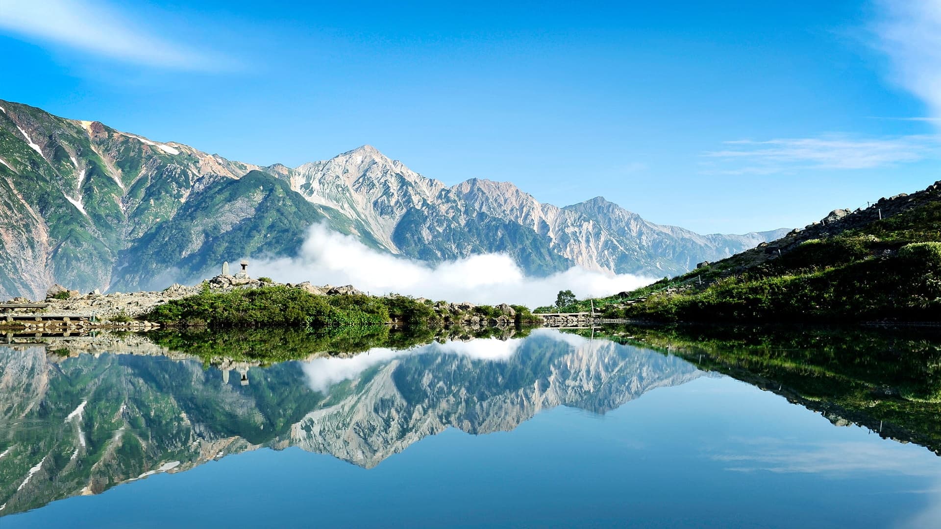 Tsugaike Nature Park boardwalk trail across a still alpine pond, with snow-capped Hakuba peaks reflected in the water